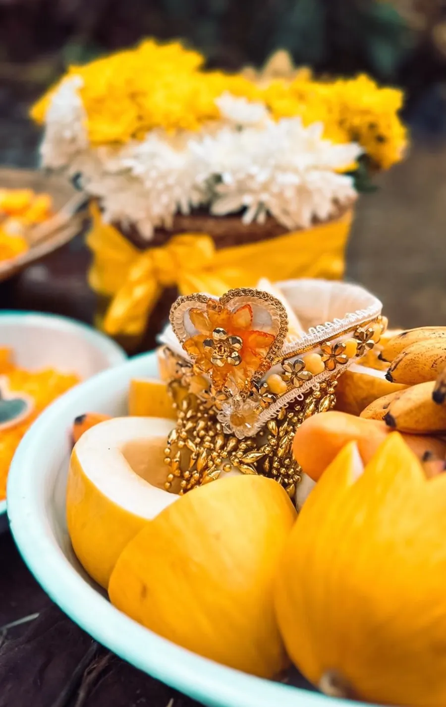 Oferenda amarela com coroa bordada em dourado, melões, bananas e flores brancas e amarelas